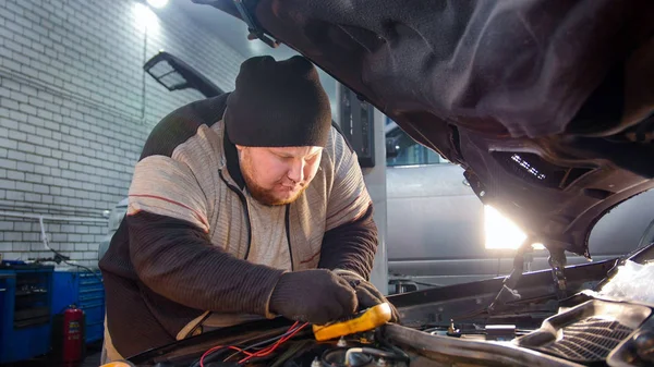 Car service. Thick mechanic man checks the voltage with a multimeter
