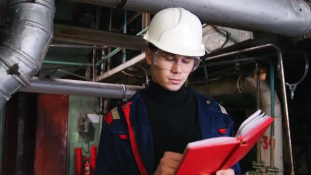 Een ingenieur van de mens in een helm maken van aantekeningen in de fabriek — Stockvideo