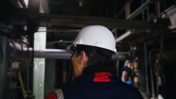 Человек-инженер в шлеме ходит по заводу и оглядывается вокруг — стоковое видео