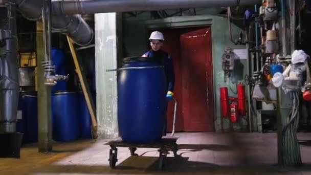 A man engineer in manufacturing plant rolls a cart with a barrel — Stock Video