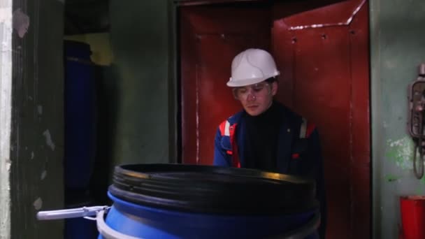 Een ingenieur van de mens het dragen van een helm in de fabriek rolt een kar met een leeg vat — Stockvideo