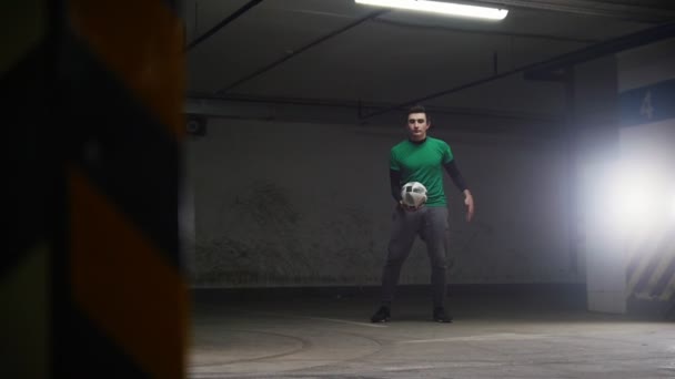 Aparcamiento subterráneo. Hombre de fútbol atlético entrenando sus habilidades de fútbol. Patear la pelota, lanzarla al aire y atrapar la pelota en el cuello — Vídeo de stock
