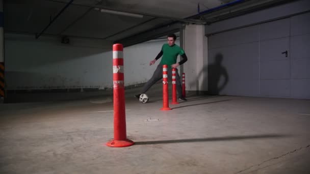 Underground parking. Athletic soccer man training his football skills. Leading the ball skirting obstacles — Stock Video