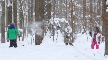 Kar kış ormandaki küçük bir çocukla oynayan iki küçük kız. Kartopu atarak