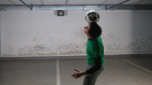 Tiefgarage. ein junger, geschickter Fußballmann, der Fußballtricks trainiert. Balancieren des Balles auf Kopf und Rücken. — Stockvideo