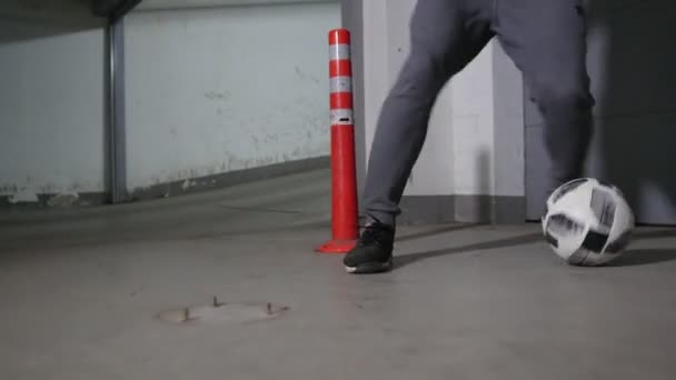 Parking souterrain. Un footballeur qui s'entraîne au football. Il mène la balle en contournant les obstacles. Gros plan — Video