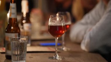 Adam bir bardak koyu bira alır ve yumuşak iç aydınlatma ile barda otururken içmeye başlar.