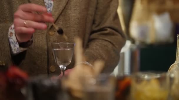 Привлекательный мужчина с рыжей бородой пьет оливку с коктейлем, разговаривает с кем-то и смеется в баре с мягким внутренним освещением. . — стоковое видео