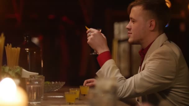 Hombre atractivo está bebiendo licor rojo con limón y sonriendo en la barra con iluminación interior suave . — Vídeos de Stock