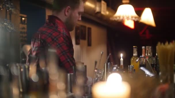 Jeune barman professionnel versant une boisson rouge dans le verre du bar avec un éclairage intérieur doux . — Video