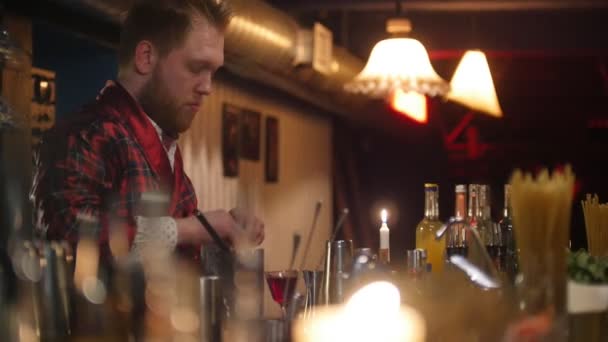 Young professional bartender wearing red apron putting a lemon into a glass with red liquor — Stock Video