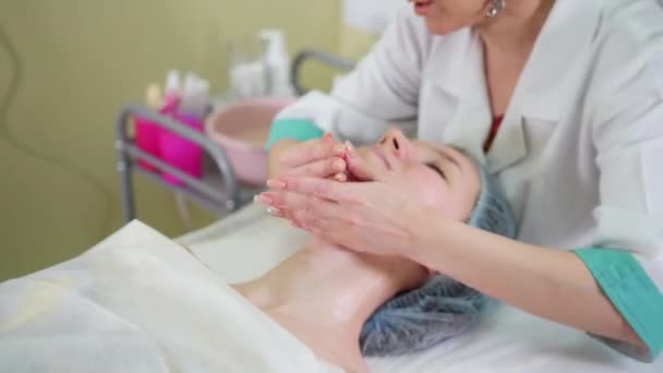 A face massage treatment in cosmetology clinic. A woman beautician gently massaging the woman chin — Stock Video