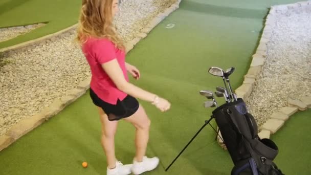 Je joue au mini-golf. Une jeune femme blonde vient au sac et prend un bâton de golf — Video