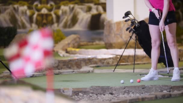 A young woman playing mini golf. A woman hitting the golf balls several times — Stock Video