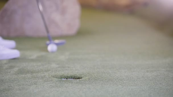 Гра в міні-гольф. Людина потрапляє в м'яч для гольфу і пропускає отвір — стокове відео
