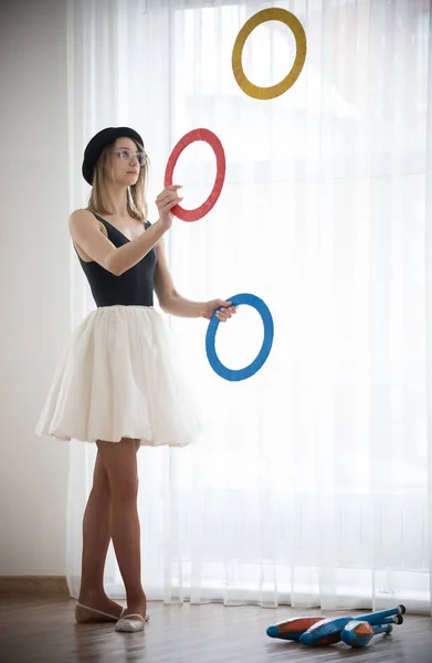 Girl in a hat juggles with rings in the studio side view