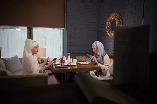 Jonge moslimvrouw zitten in cafe met haar vriend. Vergadering in hun telefoons — Stockfoto