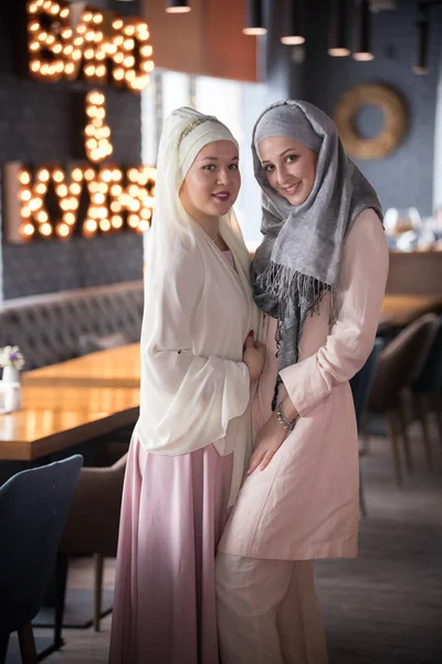 Twee jonge lachende Moslimvrouwen permanent in het café — Stockfoto