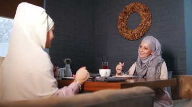 Bir restoranda oturan iki Müslüman kadın. Bir garson sipariş getiriyor. Orta atış
