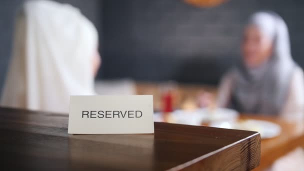 Reserviertes Schild auf dem Tisch. zwei muslimische Frauen, die im Hintergrund sitzen und reden. eine Person entfernt das Schild vom Tisch — Stockvideo