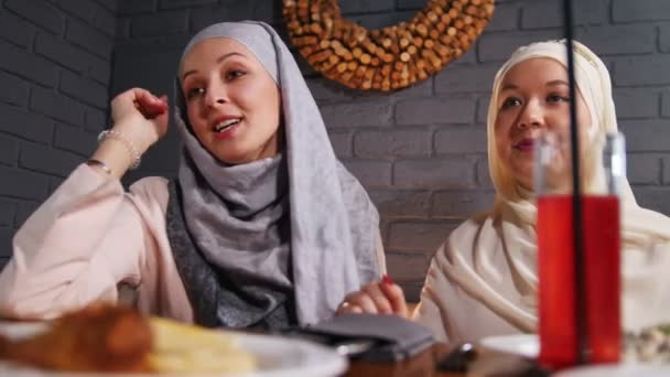 Zwei muslimische Frauen sitzen in einem Restaurant und unterhalten sich mit ihrem Freund — Stockvideo