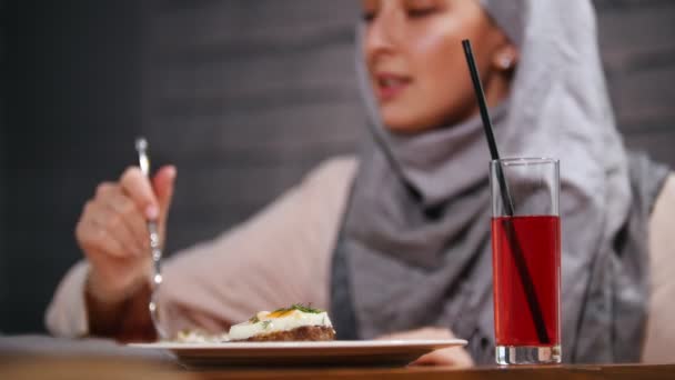 Una mujer musulmana sentada en un restaurante comiendo un plato y bebiendo jugo — Vídeos de Stock