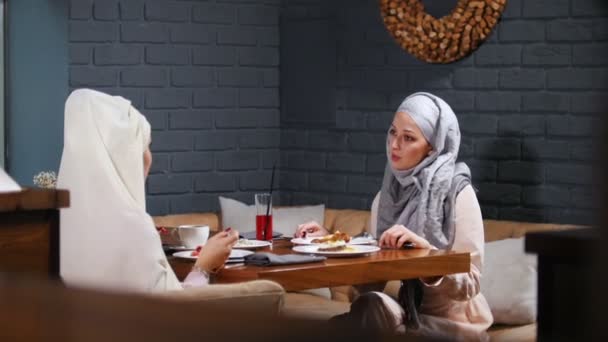 Мусульманка сидить у кафе, їсть посуд і розмовляє — стокове відео
