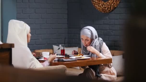 Eine muslimische Frau sitzt in einem Café, isst ihr Geschirr und redet — Stockvideo