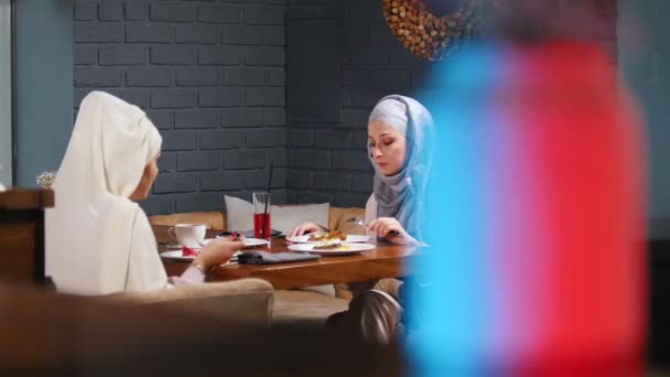 Μια μουσουλμανική γυναίκα κάθεται σε μια καφετέρια στο τραπέζι και έχοντας μια συνομιλία — Αρχείο Βίντεο