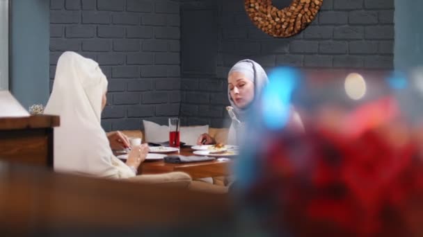 Eine muslimische Frau sitzt in einem Café am Tisch, isst und unterhält sich — Stockvideo