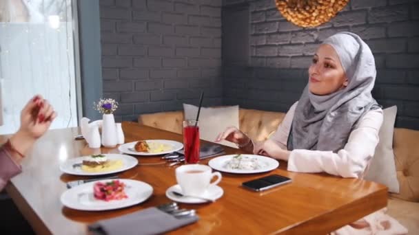 Мусульманка сидить у кафе за столом і розмовляє. Жінка вирівнює столові прибори — стокове відео