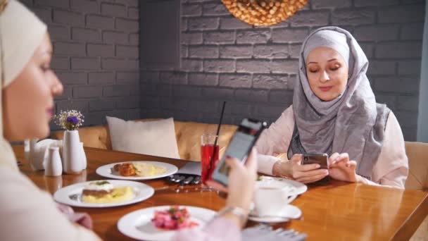 Bir restoranda bir masada oturan iki Müslüman kadınlar ve onların telefon oturmuş. Resimleri gösterme — Stok video