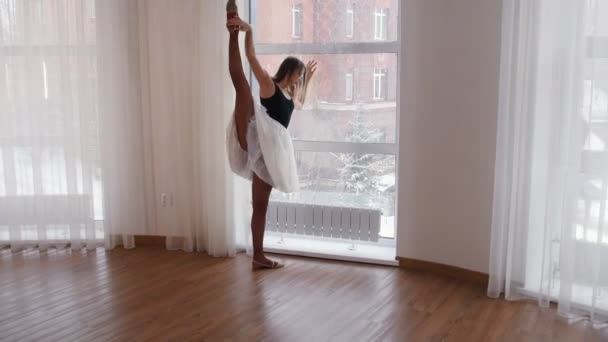 Jonge vrouw ballerina aan het warmrijden in de studio staan bij het raam — Stockvideo