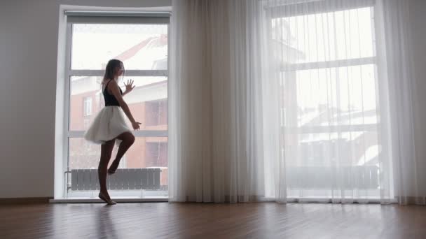 Молода балерина стоїть біля вікна і тренує свій танець — стокове відео