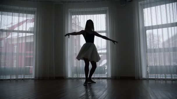 Студия в сумерках. Силуэт молодой женщины-балерины, исполняющей изящное вращение — стоковое видео