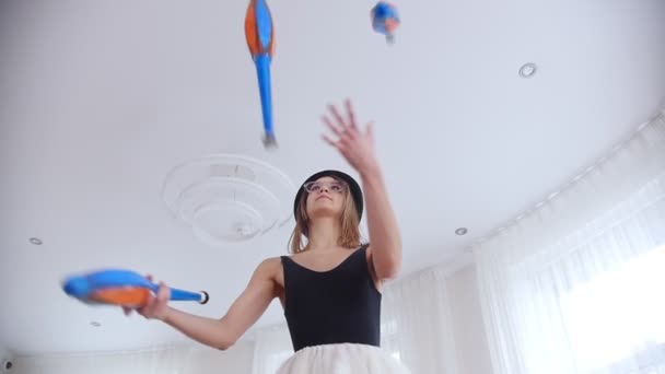 Молодая женщина в черной шляпе тренируется жонглировать в яркой студии — стоковое видео