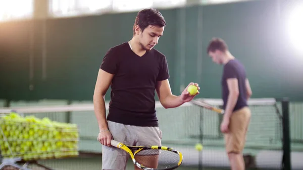 Entraînement sur le terrain de tennis. Des jeunes hommes s'entraînent. Un homme tenant une balle — Photo