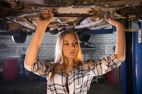 Jonge sexy mechanic vrouw permanent onder de auto in auto reparatieservice. Op zoek naar de kant — Stockfoto
