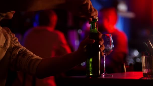 Bar con iluminación de neón. Un hombre abre una botella de cerveza y la vierte en el vaso — Vídeos de Stock