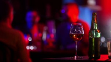 Neon aydınlatma çubuk. Genç bir adam yeşil şişe, bardak bira ve oturup arkadaşları yanında alır. Alkış