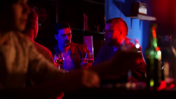 Bar com iluminação de néon. Companhia de amigos a passar tempo juntos. Um jovem em primeiro plano bebendo cerveja — Vídeo de Stock