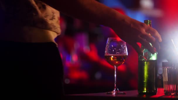 Bar met neon verlichting. Een jonge man neemt de groene fles bier en zitten naast zijn vrienden. Cheers — Stockvideo