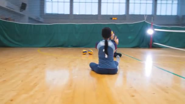 Sport für Behinderte. zwei junge Frauen, die in der Sporthalle auf dem Boden sitzen und mit einem Ball spielen — Stockvideo