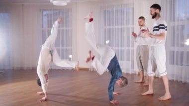 Dövüş sanatları. İki akrobatik adam performans gösteren capoeira öğeleri ve öğrencilerinin onları izliyor