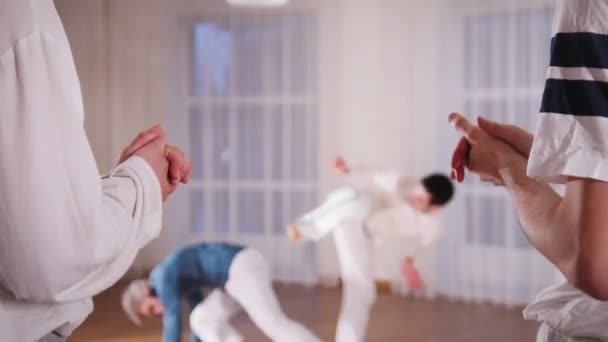 Artes marciales. Dos hombre acrobático realizando elementos de capoeira mientras sus estudiantes aplaudiendo de la mano — Vídeos de Stock