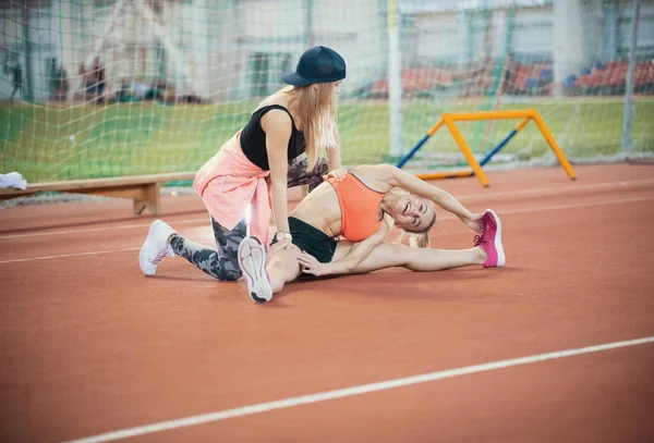 Two young beautiful women with blonde hair doing exercises and breathing hard in the sports hall — Stock Photo, Image