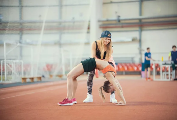 Two young women with blonde hair doing exercises and breathing hard in the sports hall together — Stock Photo, Image