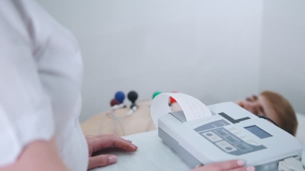 Une clinique médicale. Un homme qui reçoit un ECG. Une bande de résultats sortant de la machine — Video