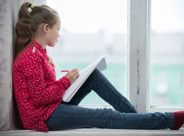 Une petite fille assise sur un rebord de fenêtre et regardant par la fenêtre — Photo