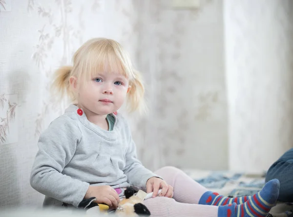 Маленькая блондинка, сидящая на кровати — стоковое фото